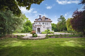 A large, two-story house with a symmetrical facade, a central entrance, and a formal garden with a circular flower bed.