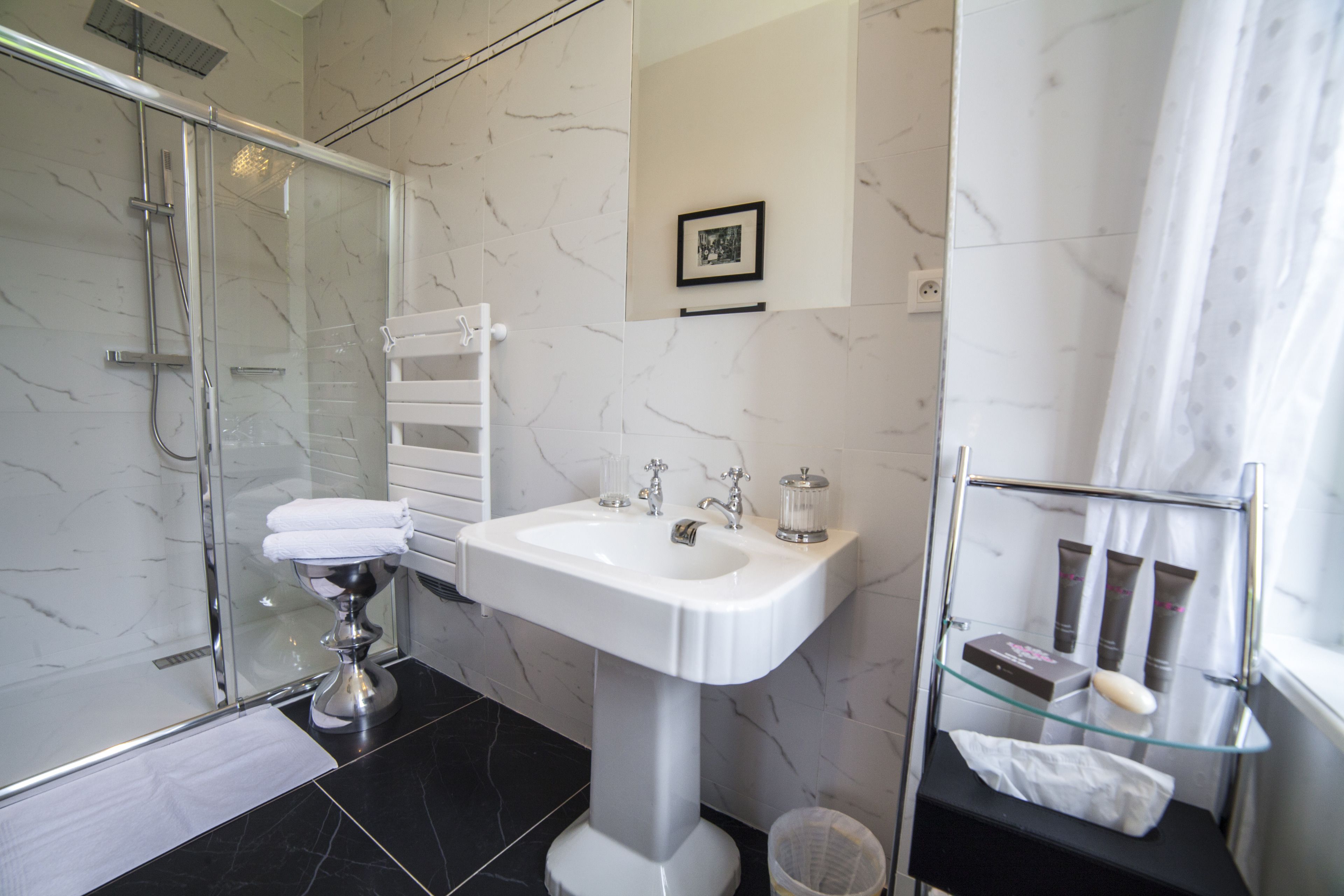 Un bany modern amb una dutxa de mampara de vidre, un lavabo de pedestal i una prestatgeria de vidre amb productes de tocador.