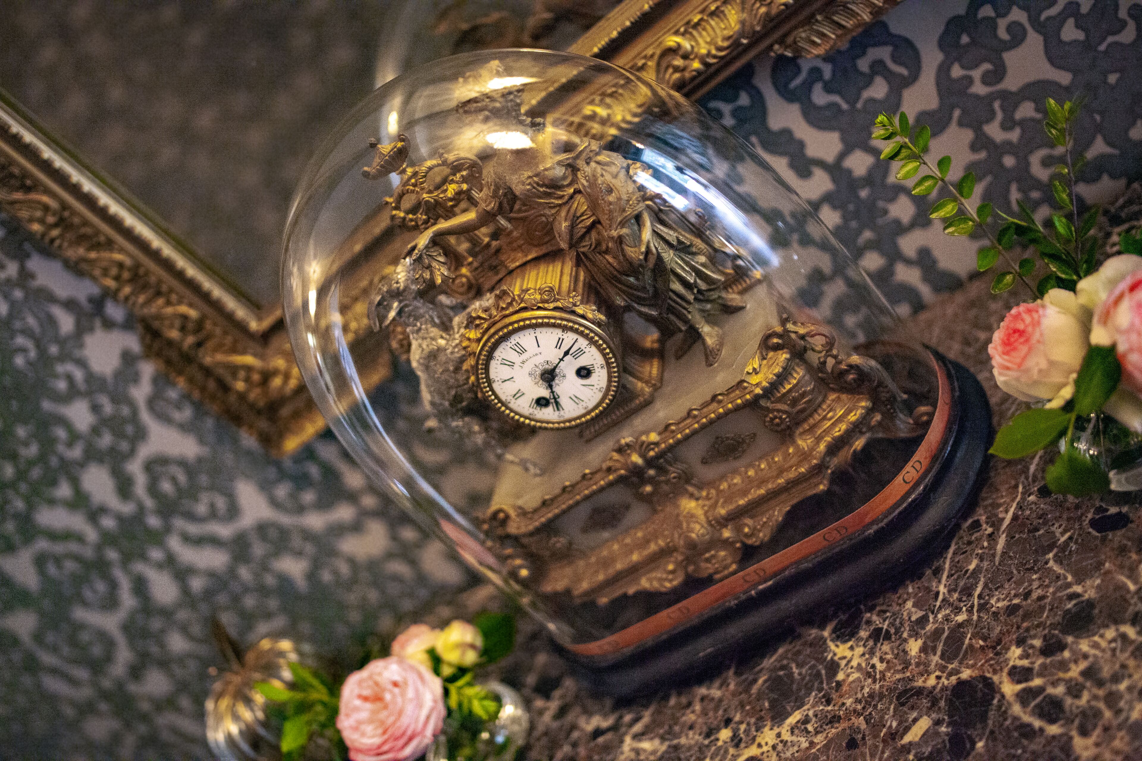 Un orologio vintage con cupola in vetro, design elaborato e decorazioni floreali.