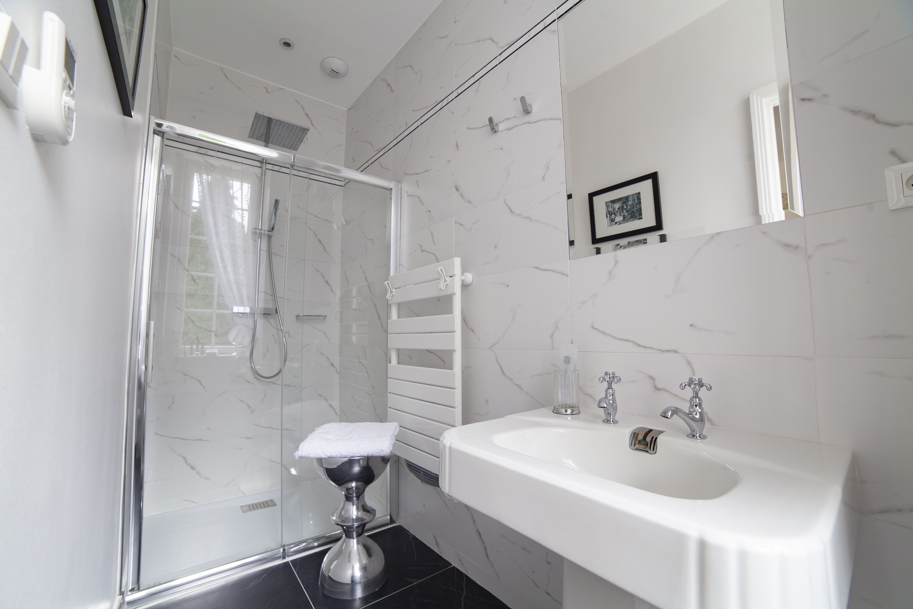 A modern bathroom with a glass-enclosed shower, a white sink, and a marble-tiled wall.