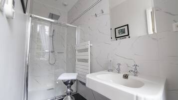 A modern bathroom with a glass-enclosed shower, a white sink, and a marble-tiled wall.