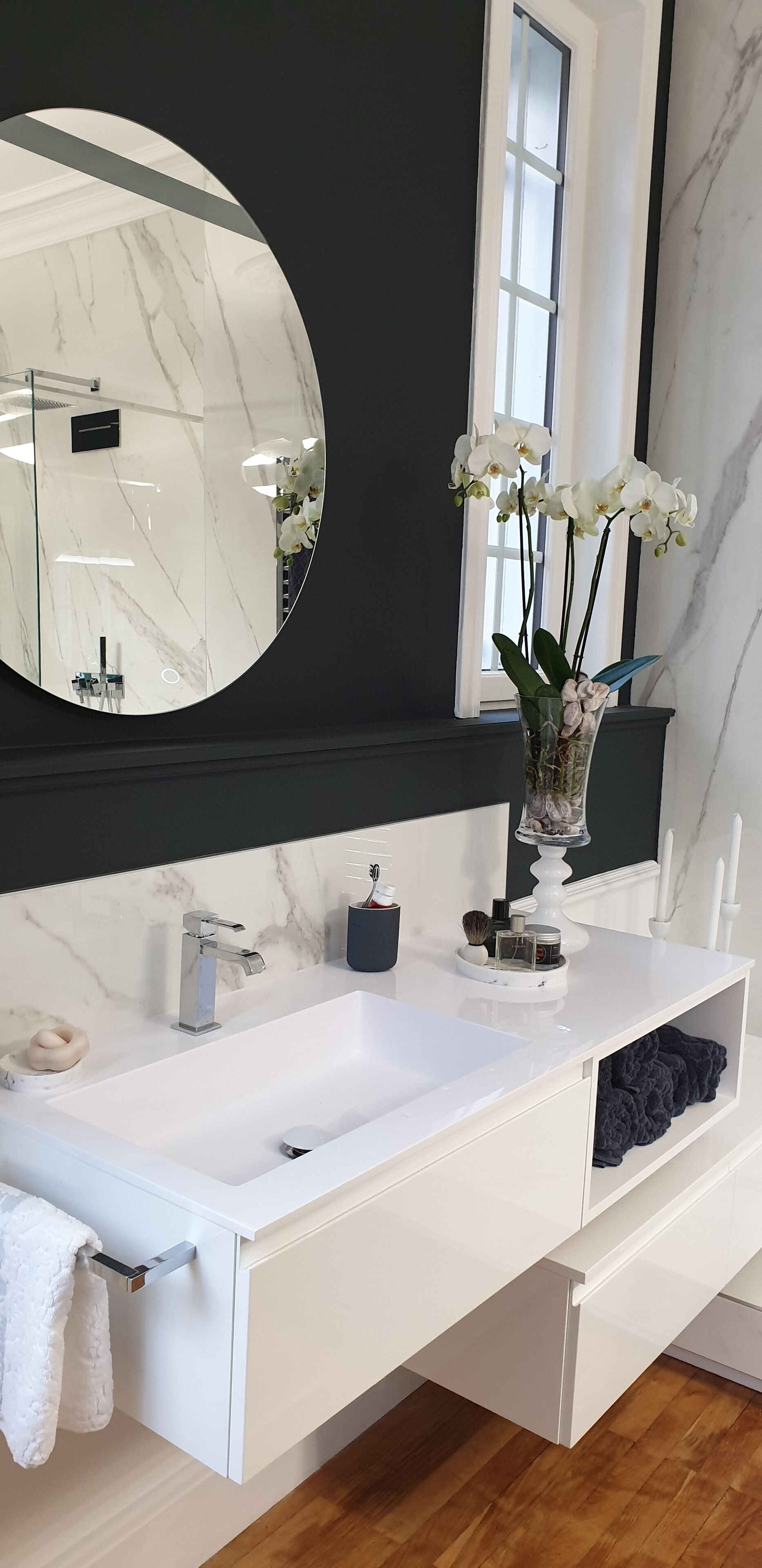 A modern bathroom with a white vanity, a large mirror, and a vase of white orchids.