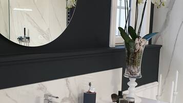 A modern bathroom with a white vanity, a large mirror, and a vase of white orchids.