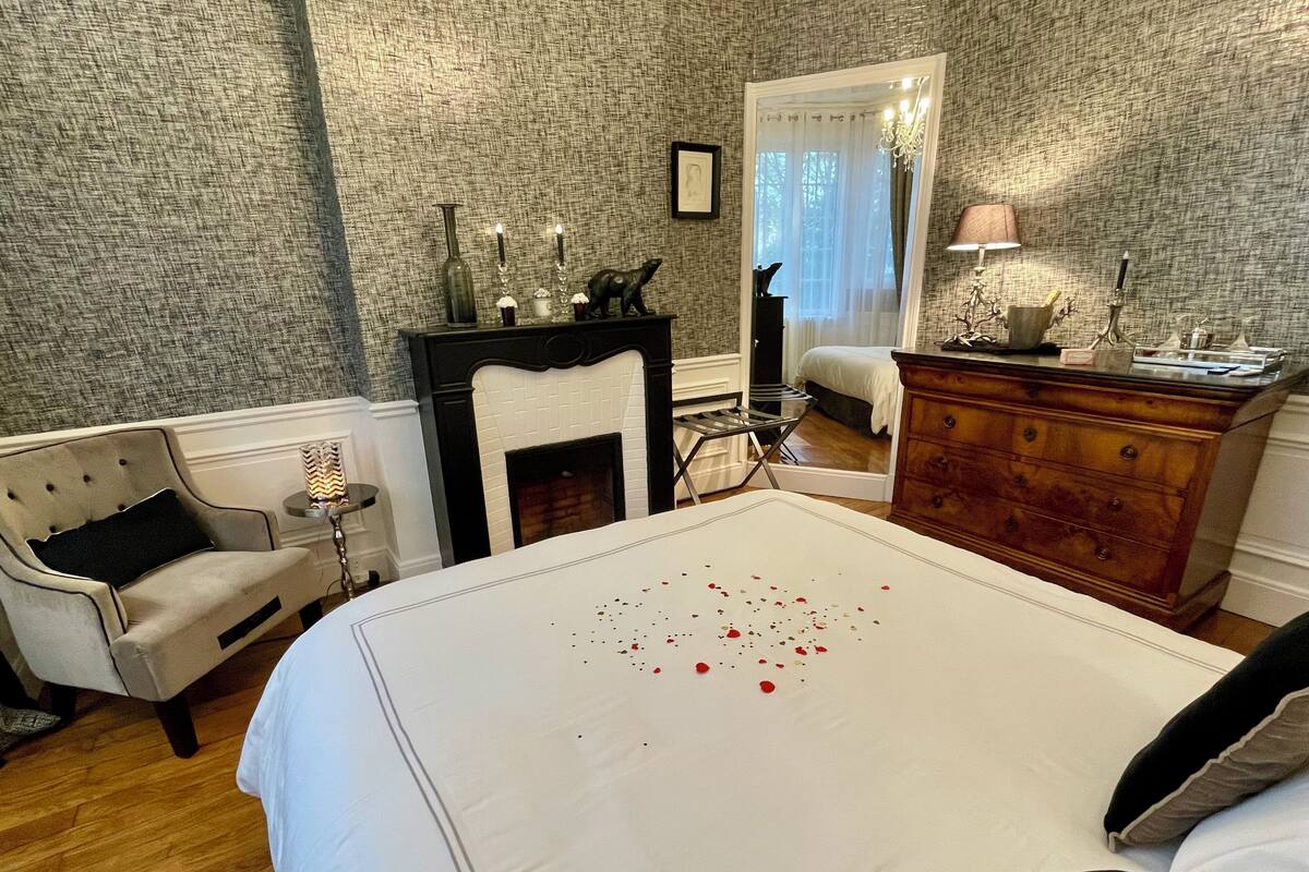A bedroom with a large bed, a fireplace, a dresser, and a mirror.