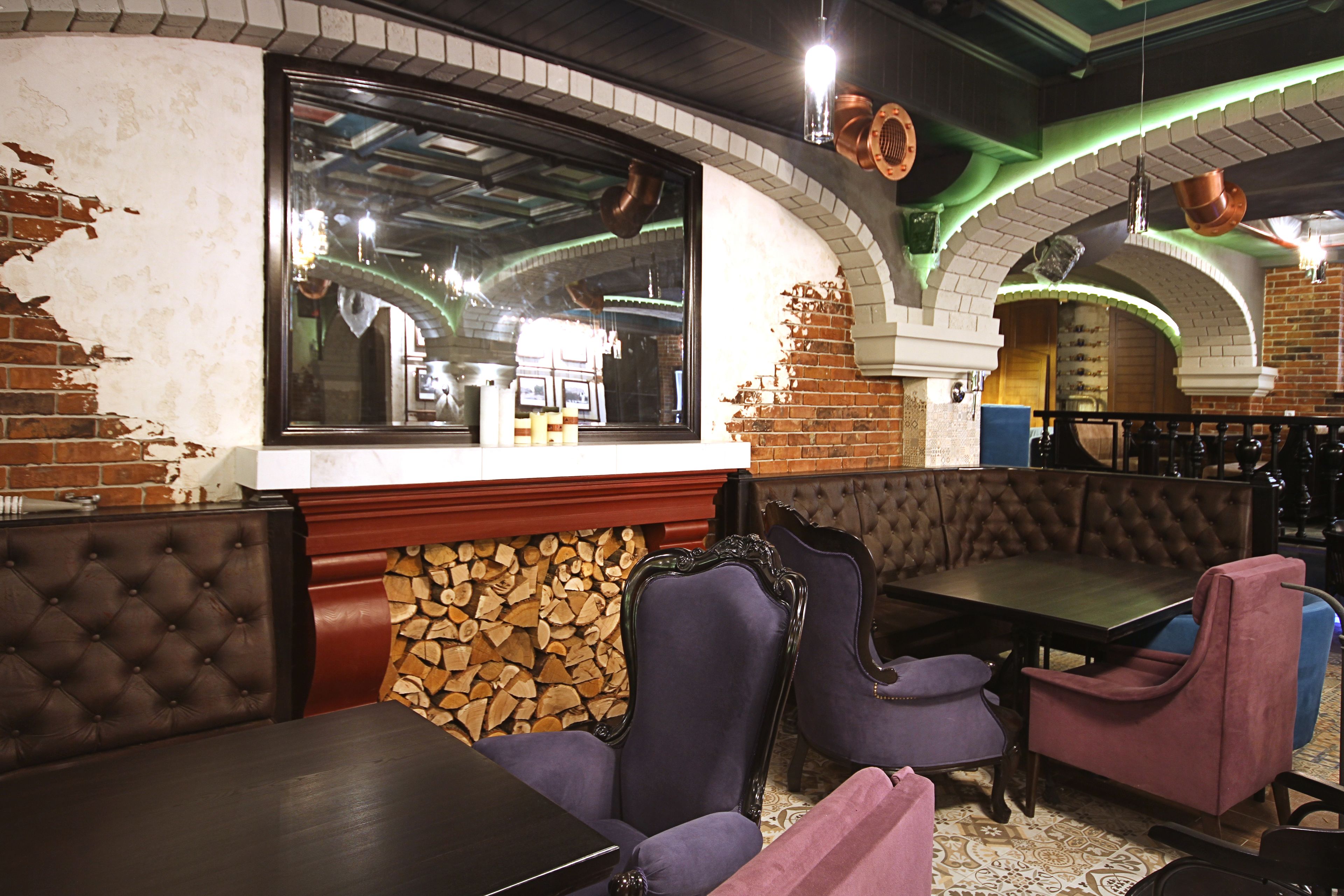Interior de restaurante con paredes de ladrillo, un ventanal grande y una combinación de asientos tapizados en tonos morado y marrón.