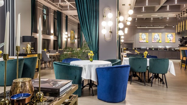 Ein moderner Essbereich mit sesseln in blau-grünem Stoff, einem runden Tisch und einer Bar mit einer Theke und Hockern.