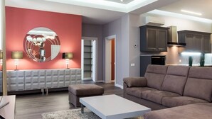 Ein modernes Wohnzimmer mit einer Couch, einem Hocker und einem Couchtisch. Es gibt eine Küchenzeile mit Schränken und einem Herd.