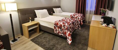 A hotel room with two beds, a desk, a TV, and a lamp.