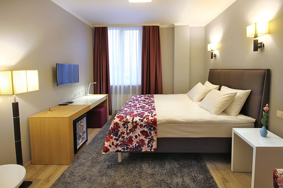 Une chambre d’hôtel comprenant un lit, une table de chevet, un bureau, une télévision et des rideaux.