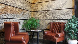 Ein Eckzimmer mit einer Chandelüster, zwei Ledersesseln, einem Tisch und einem Blumentopf.