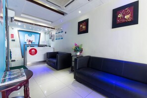 A reception area with a reception desk, black leather sofas, a small table with a vase of flowers, and framed artwork on the walls.