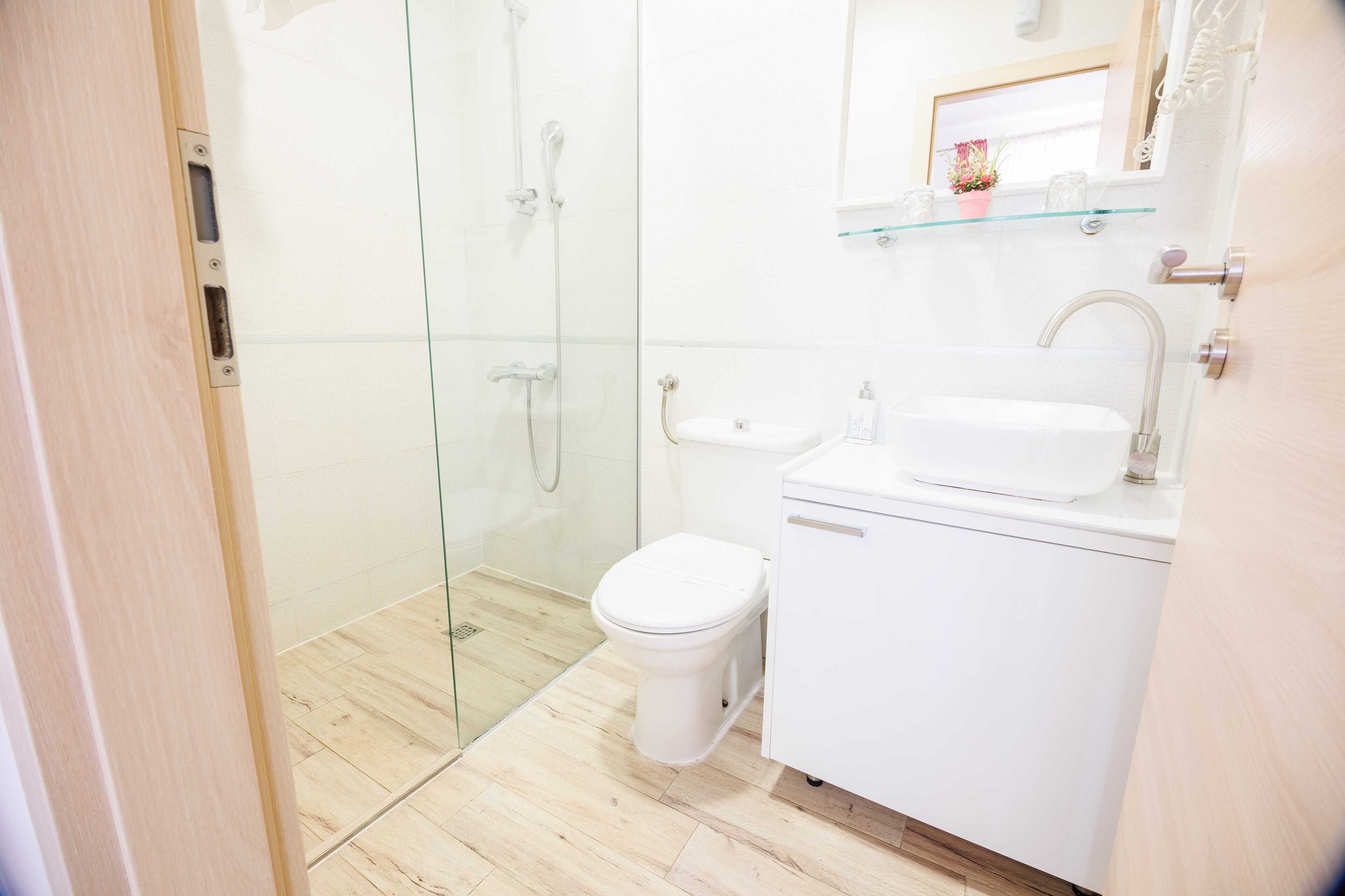 A modern bathroom with a glass shower enclosure, a white toilet, and a sink with a glass shelf above it.