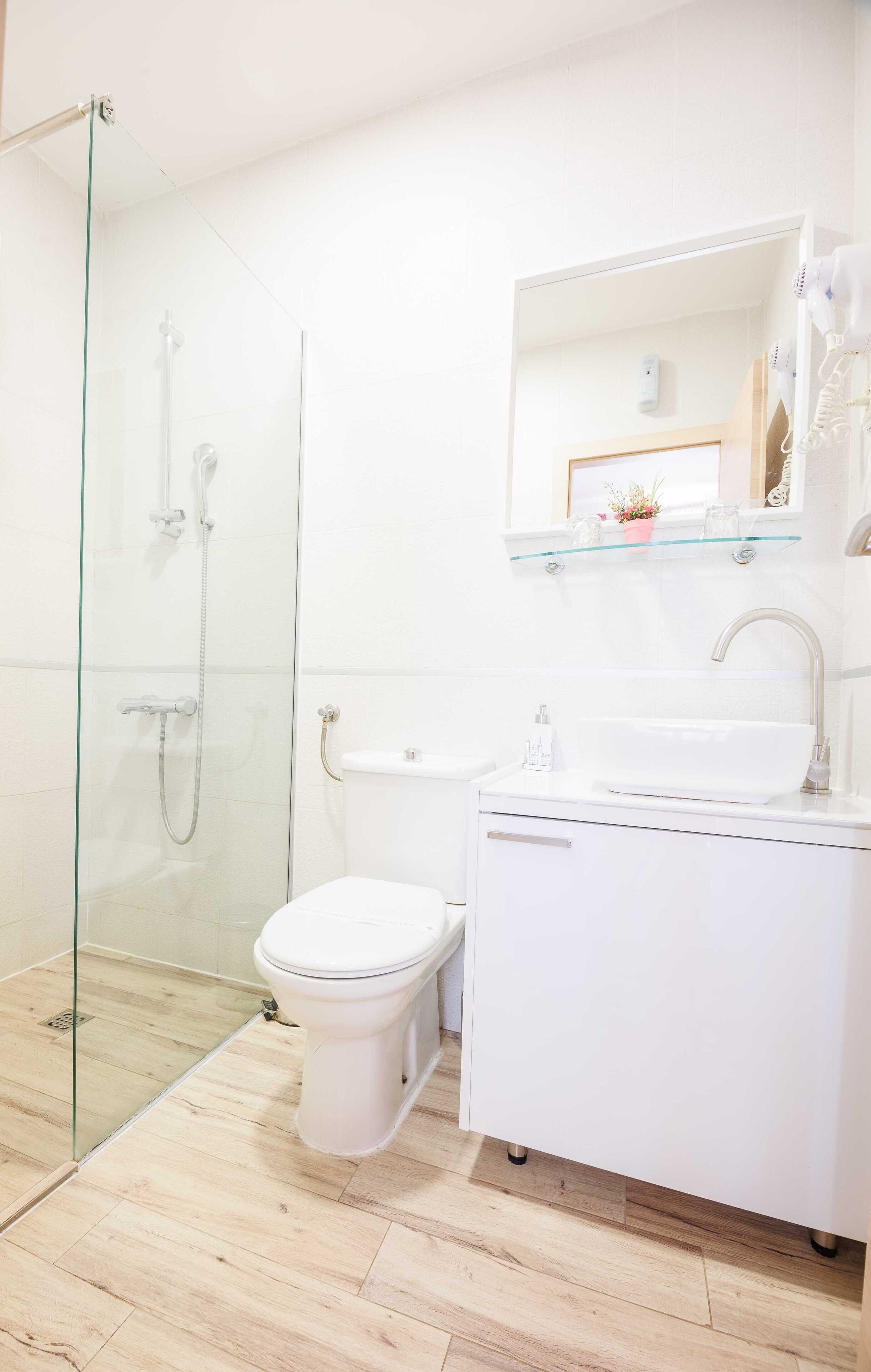 A modern bathroom with a glass shower enclosure, a white toilet, and a white sink with a mirror above.