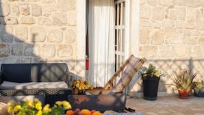 Un espace extérieur aménagé avec un mur en pierre, une table recouverte d’une nappe bleue, un canapé en osier et des plantes en pot.