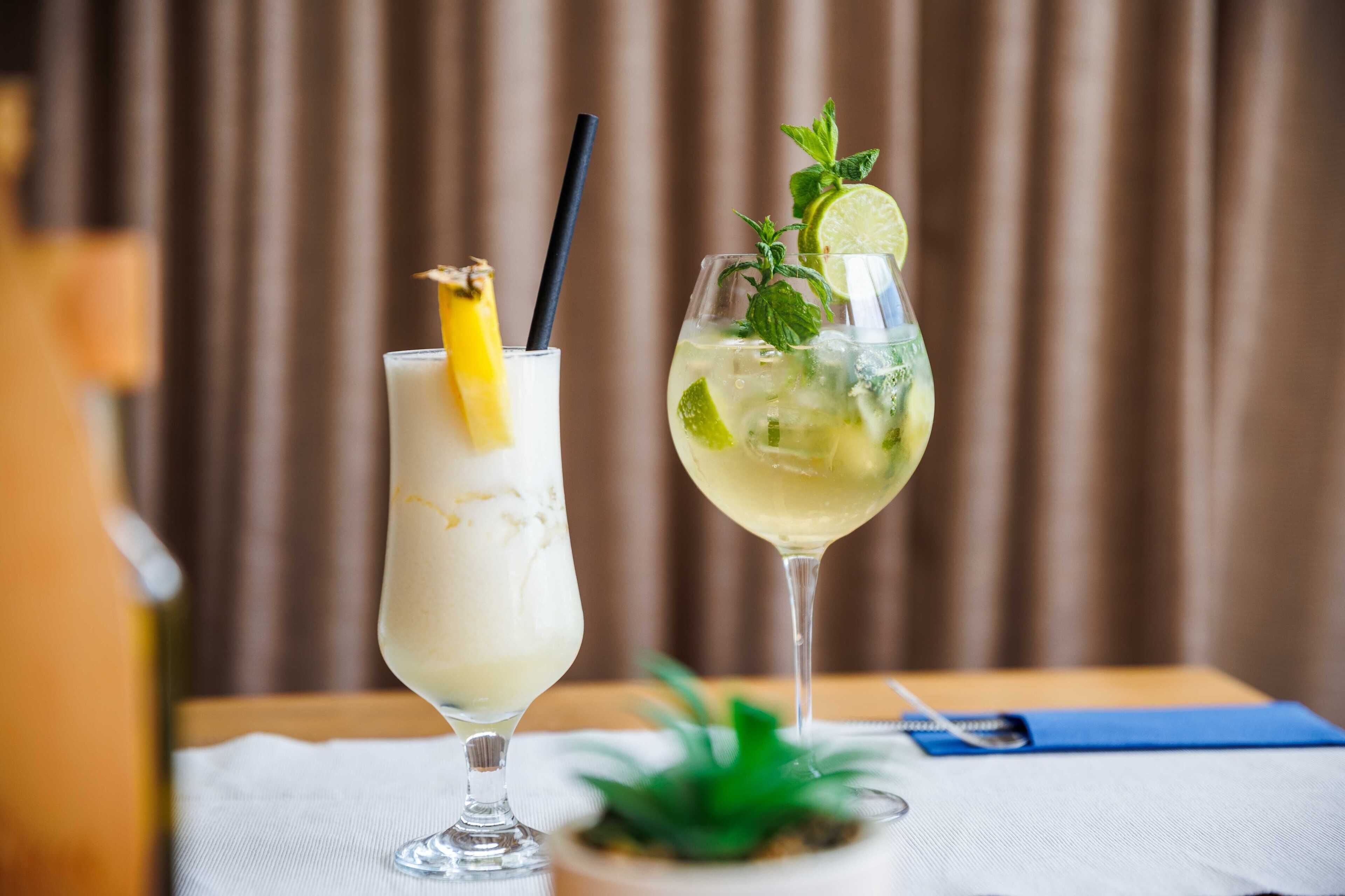 Two cocktails on a table with a plant and a blue napkin.