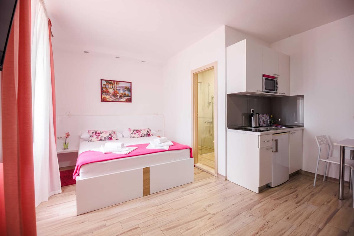 Un dormitorio con cama, mesita de noche, ducha y kitchenette equipada con microondas y fregadero.