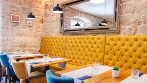 Un restaurant aux murs de pierre, avec des banquettes rembourrées de couleur jaune, des tables en bois et des chaises bleues.