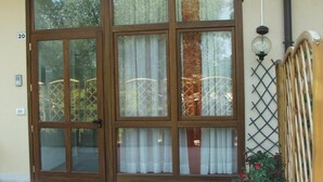 Entrada de un edificio con un amplio ventanal, una reja de metal y una maceta con flores rojas.