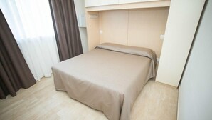 Una cama bien tendida en una habitación con piso de madera clara y pared blanca.