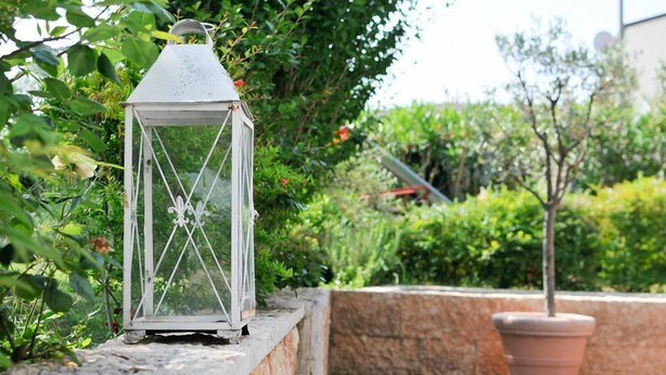 Un farol blanco sobre un alféizar de piedra con una planta en maceta cerca.