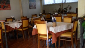 Un comedor con mesas y sillas de madera, cubiertas con manteles blancos.