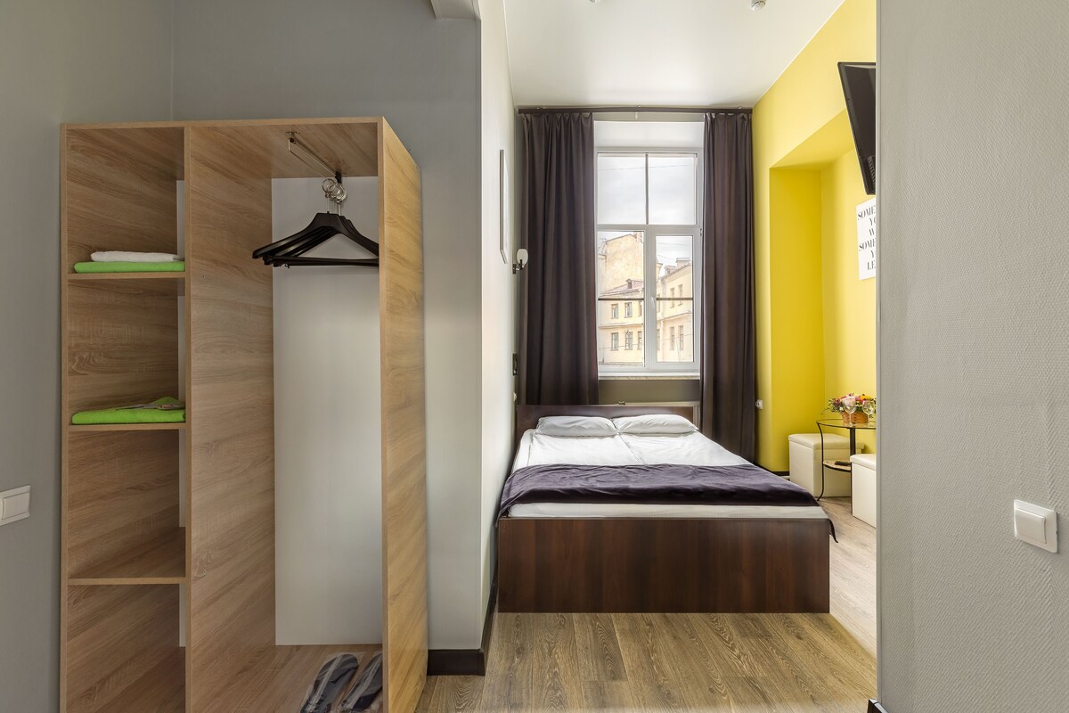 A compact bedroom with a bed, a wooden wardrobe, and a window with curtains.