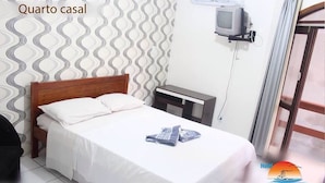 Un dormitorio con cama, televisor sobre un mueble bajo y ventana con cortinas.