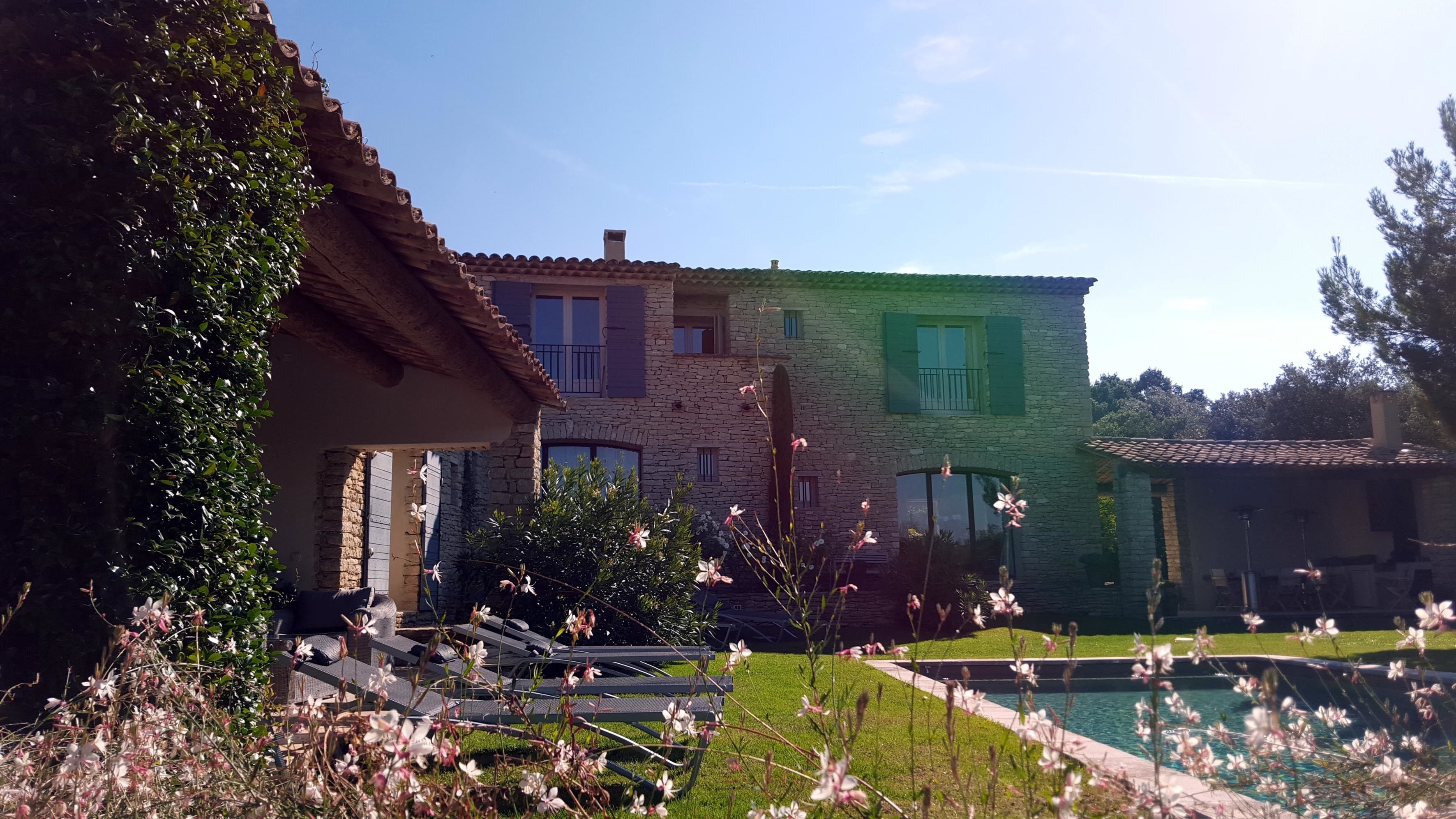 A stone building with a pool, surrounded by greenery and flowers.