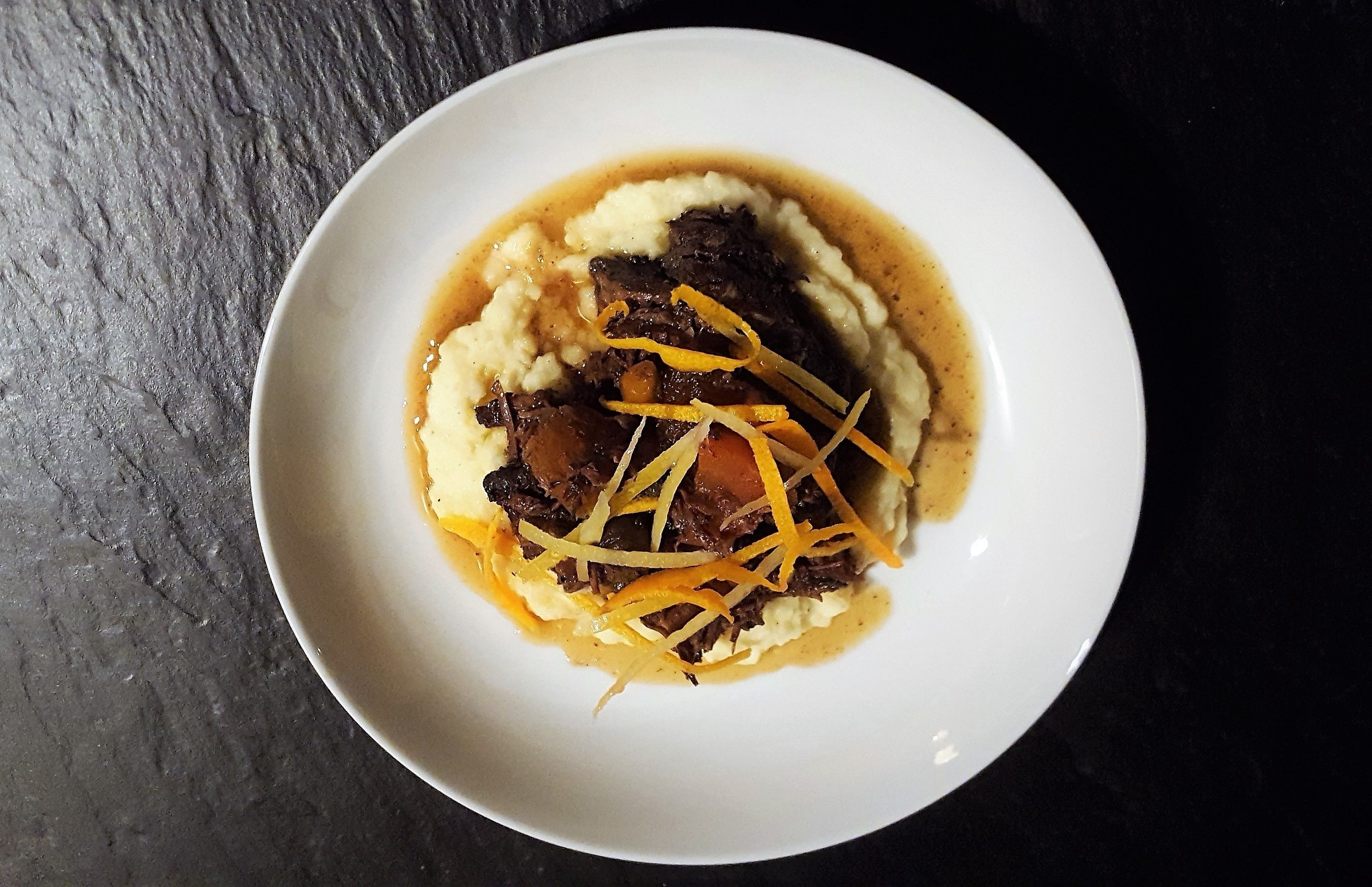 A white plate with mashed potatoes, beef, and shredded carrots on a dark surface.