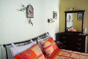 A bedroom with a bed, a dresser, a mirror, and wall decorations including a birdcage and framed pictures. - Nikolas Guesthouse (Zagori)