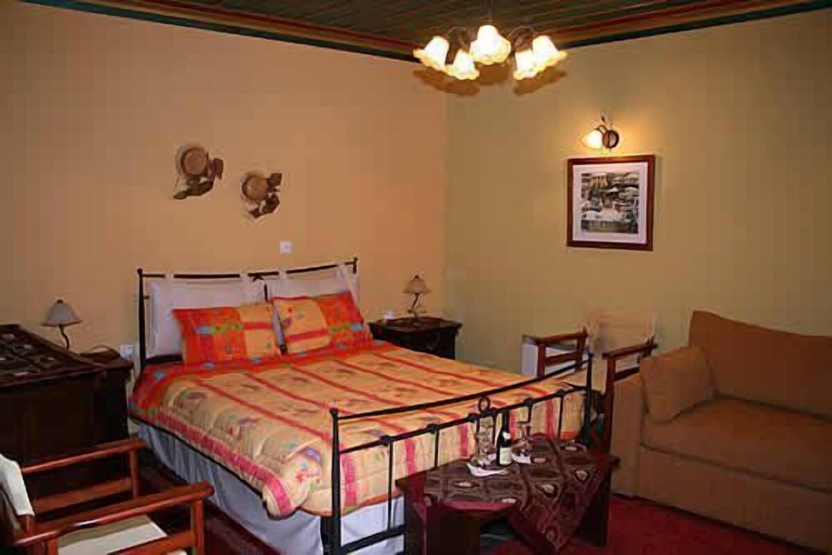 Um quarto com cama, mesa de cabeceira, luminária, cadeira e sofá.