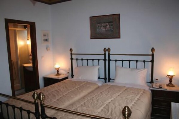 A bedroom with a bed, two bedside tables, a nightstand, a mirror, and a framed picture on the wall. - Nikolas Guesthouse (Zagori)