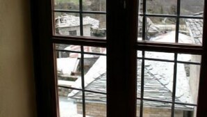 A room with a large window featuring a grid pattern, a candle holder on the windowsill, and a view of buildings and trees outside.