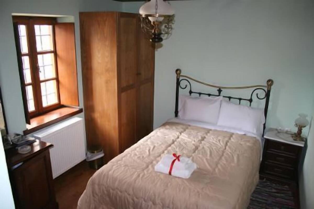 Um quarto com cama, janela, guarda-roupa e mesa de cabeceira.