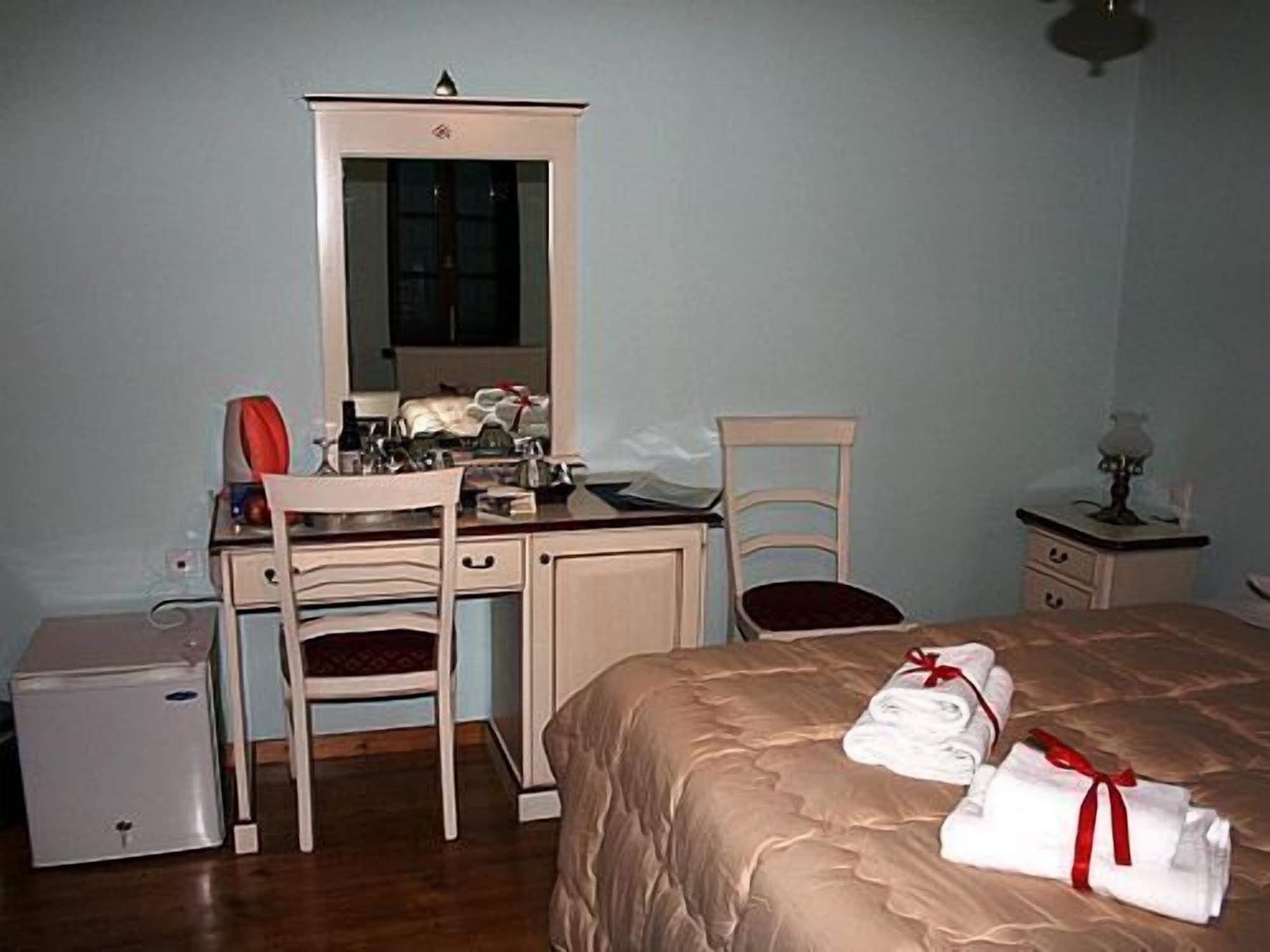 Ein Schlafzimmer mit einem Bett, einem Schreibtisch, einem Stuhl, einer Kommode, einem Spiegel, einer Lampe und einem kleinen Kühlschrank.