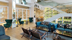 A spacious interior with a high ceiling, a central seating area with sofas and chairs, a staircase, and glass-fronted display cases. - Hotel Camiral - The Leading Hotels of the World (Caldes de Malavella)