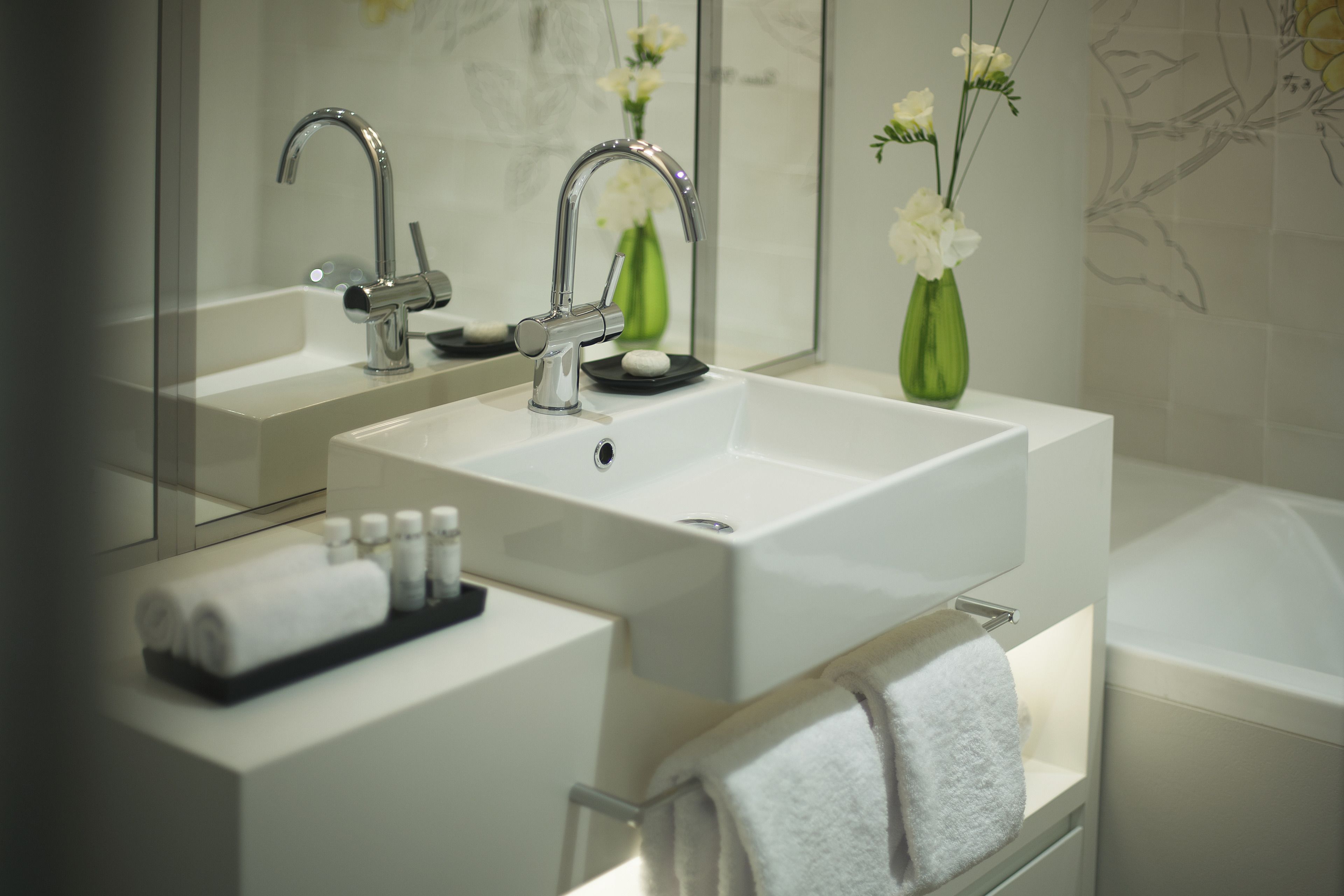 Un baño moderno con un lavabo blanco, dos grifos, un espejo y un perchero para toallas.