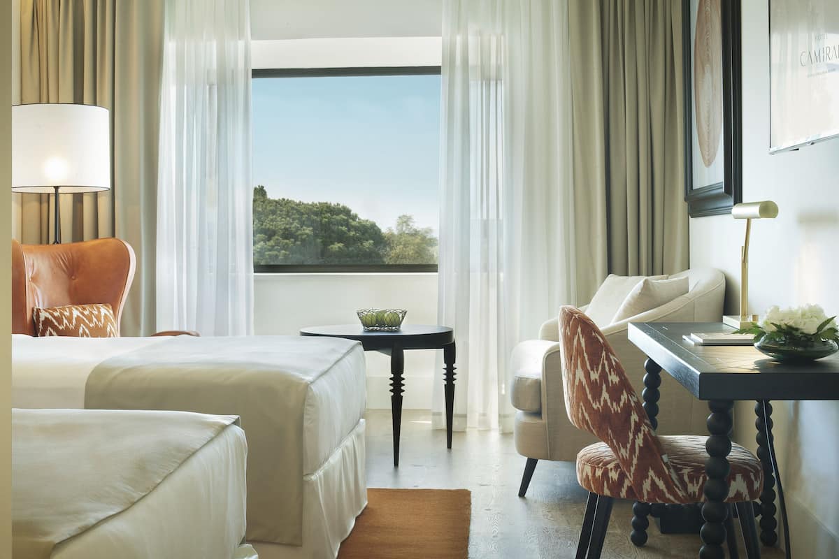 Une chambre d’hôtel avec deux lits, un bureau, une chaise, une lampe et une vue sur l’extérieur.