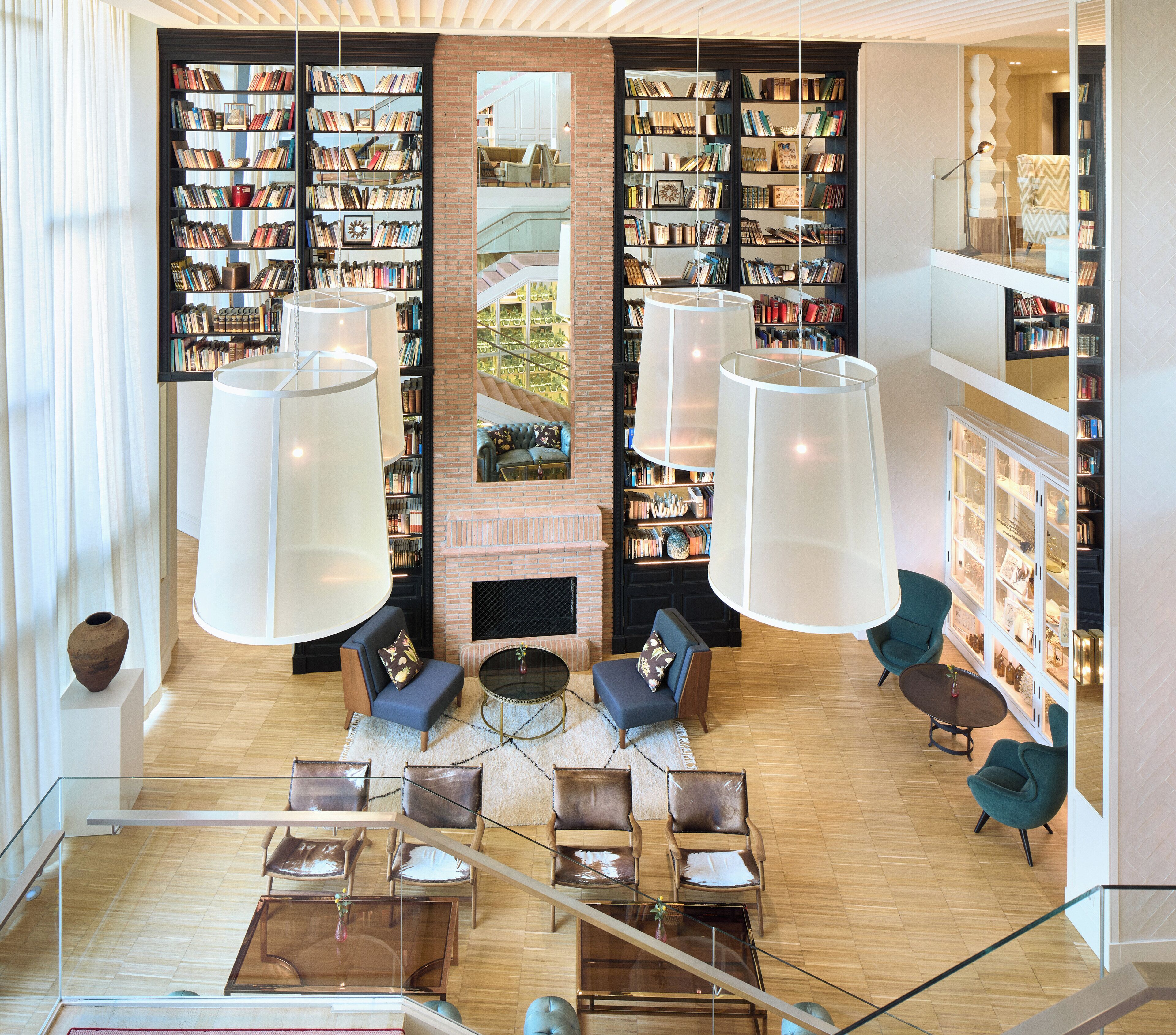 A spacious reading area with multiple bookshelves, comfortable seating, and large hanging lamps.