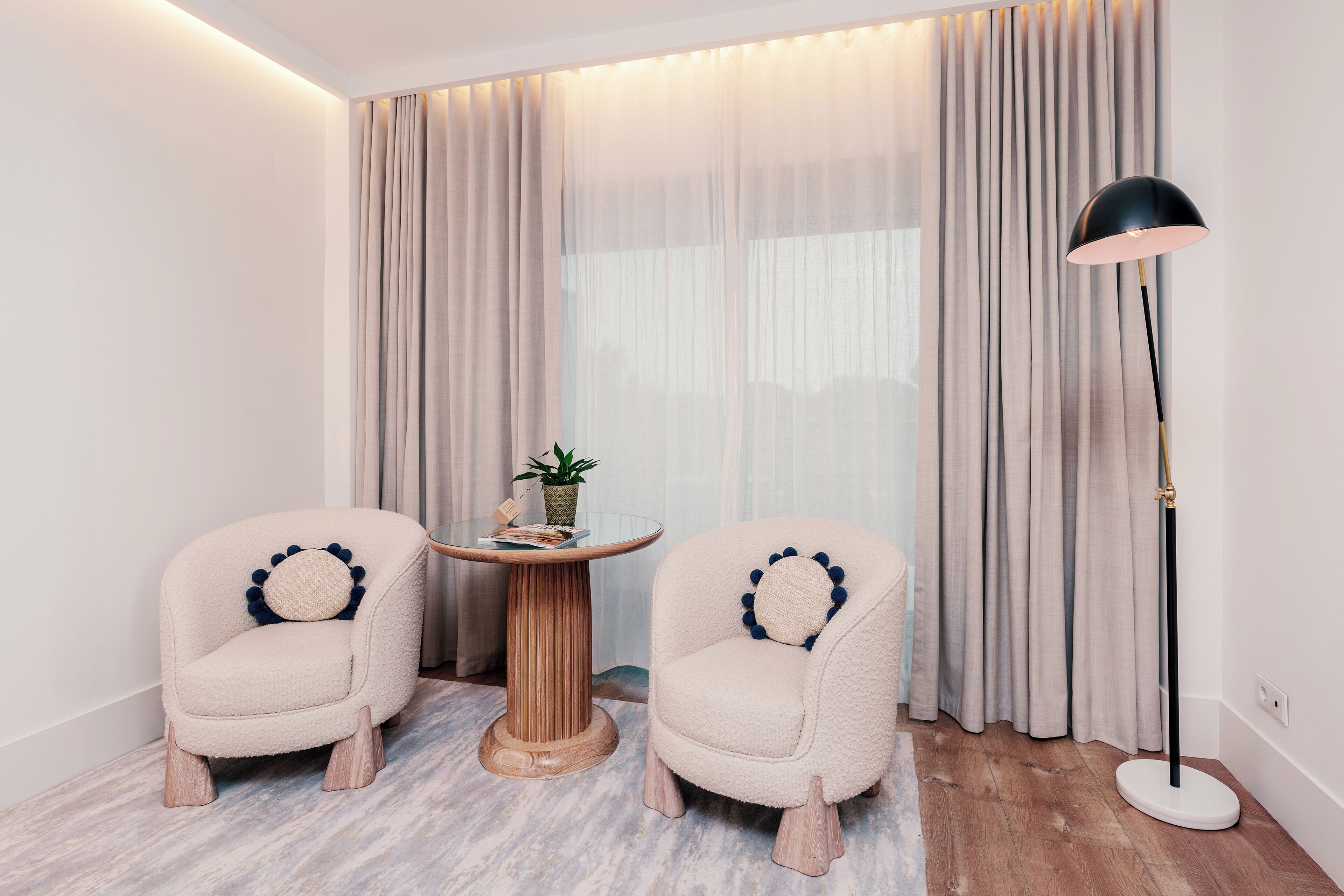 Una habitación con dos sillones cómodos, una pequeña mesa redonda con una planta y una lámpara de pie.