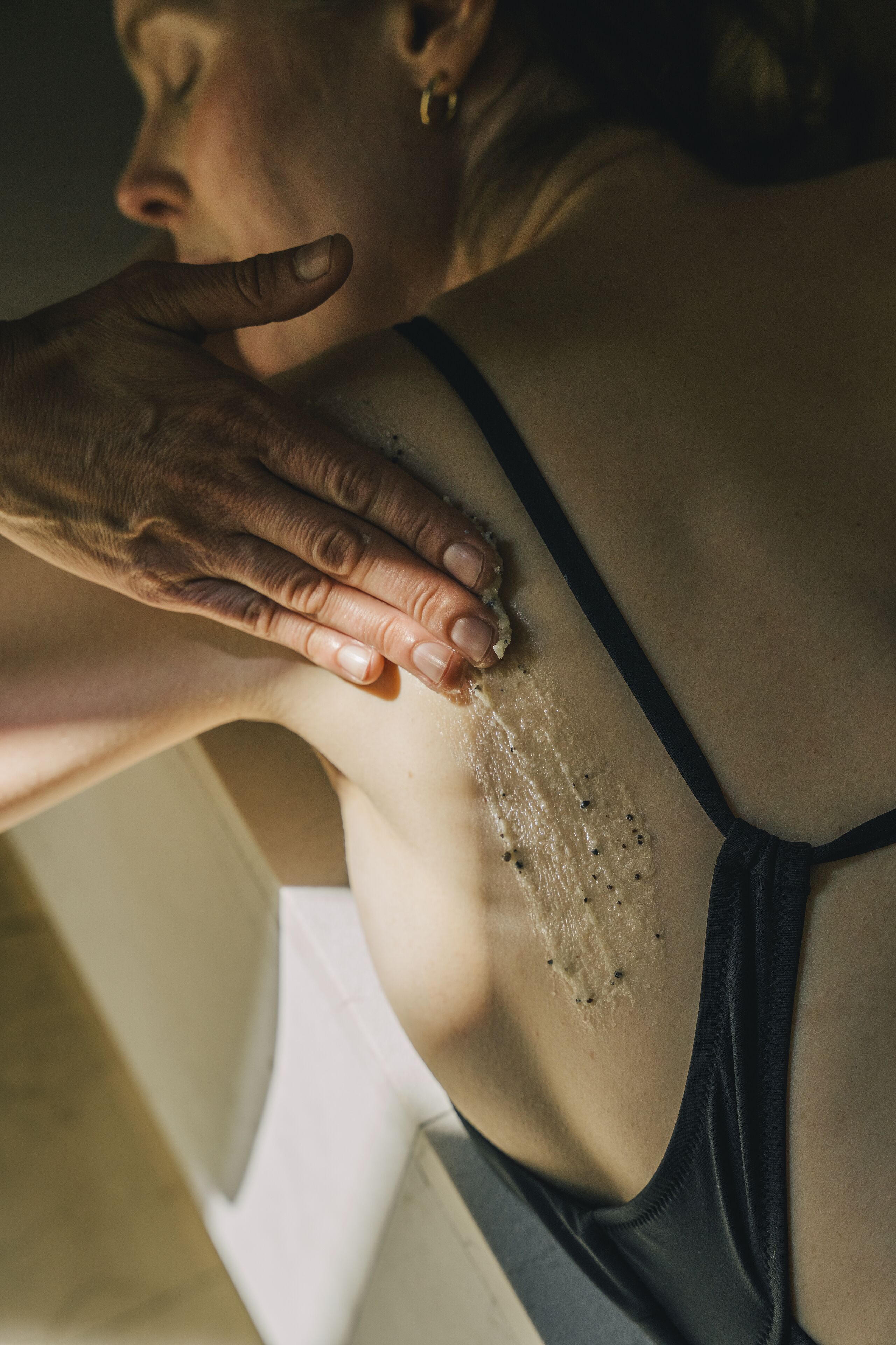 A close-up of a person's back with a hand applying a substance to the skin.