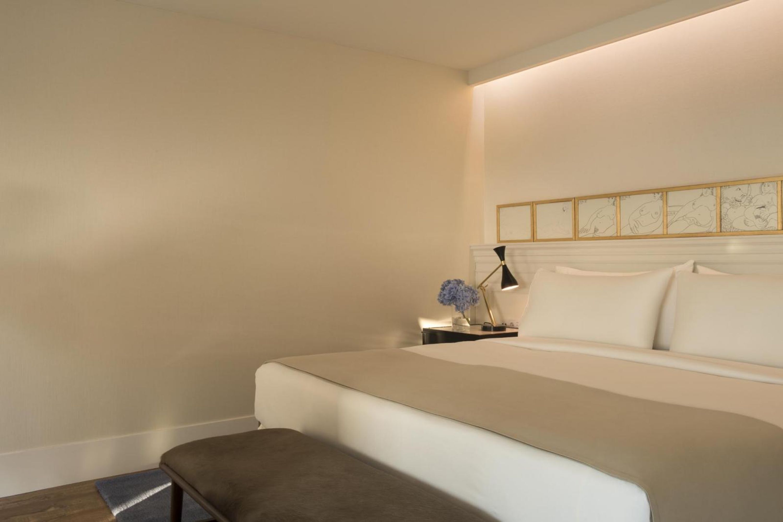 Una habitación de hotel ordenada con una cama grande, una mesita de noche con lámpara y una obra de arte colgada en la pared.