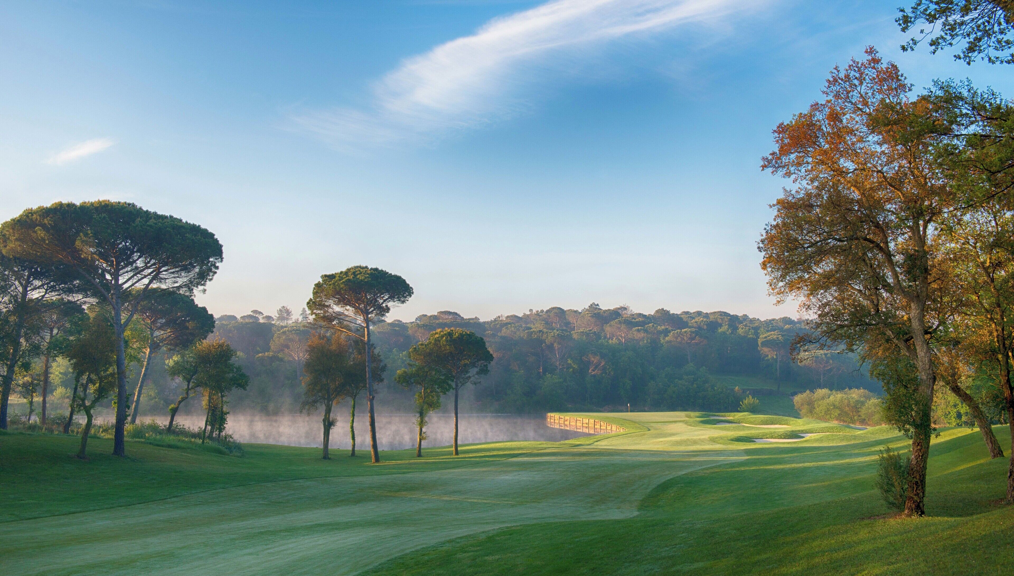 Un campo de golf con árboles, un fondo brumoso y un cielo despejado.