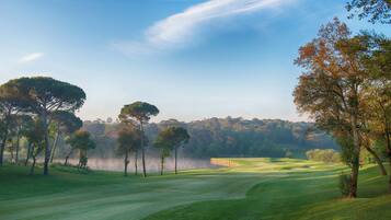 Un campo de golf con árboles, un fondo brumoso y un cielo despejado.