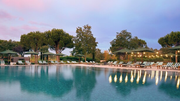A swimming pool with lounge chairs and umbrellas, surrounded by trees. - Hotel Camiral - The Leading Hotels of the World (Caldes de Malavella)