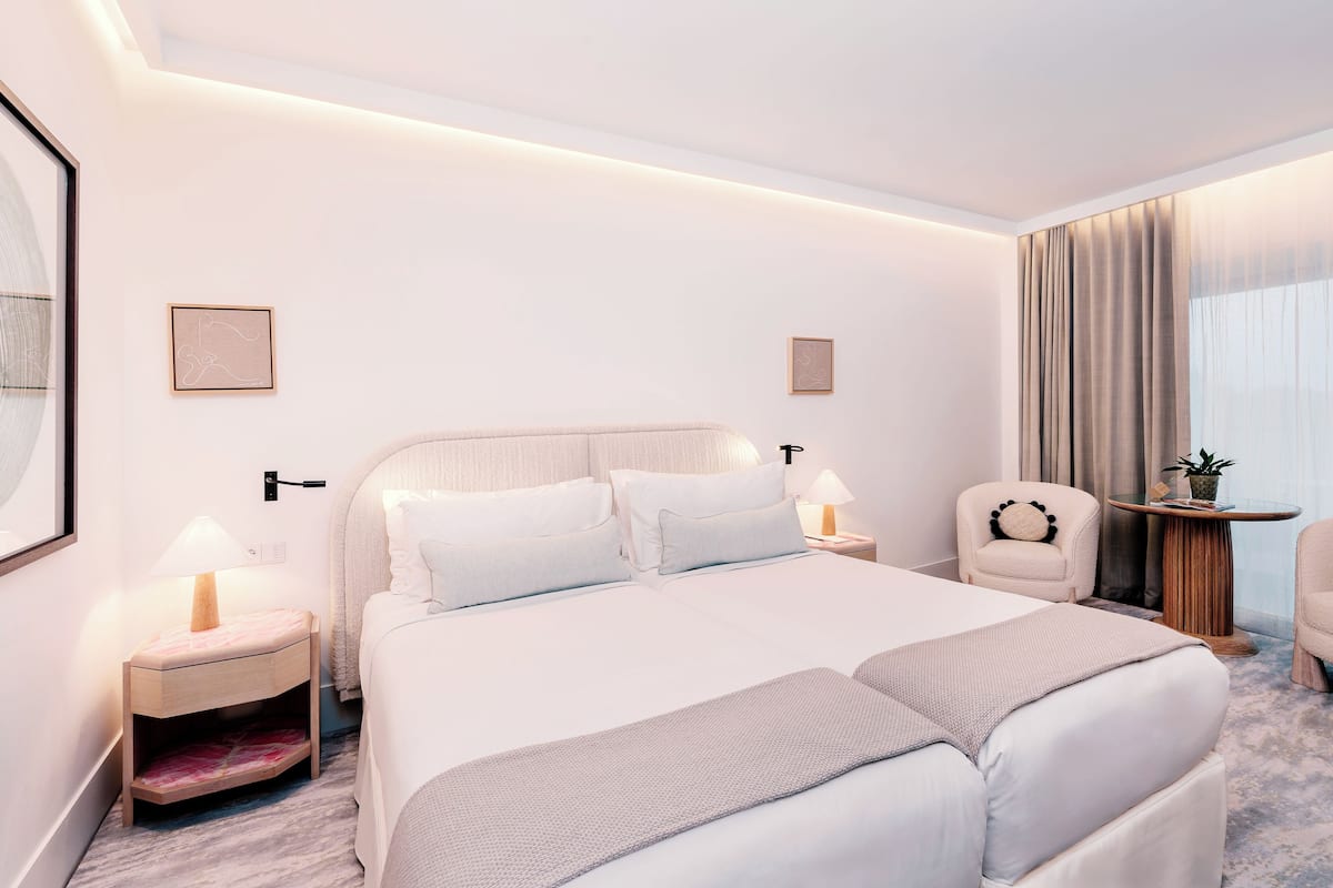 Une chambre d’hôtel moderne avec un grand lit, des tables de chevet, une chaise et une petite table agrémentée d’une plante.
