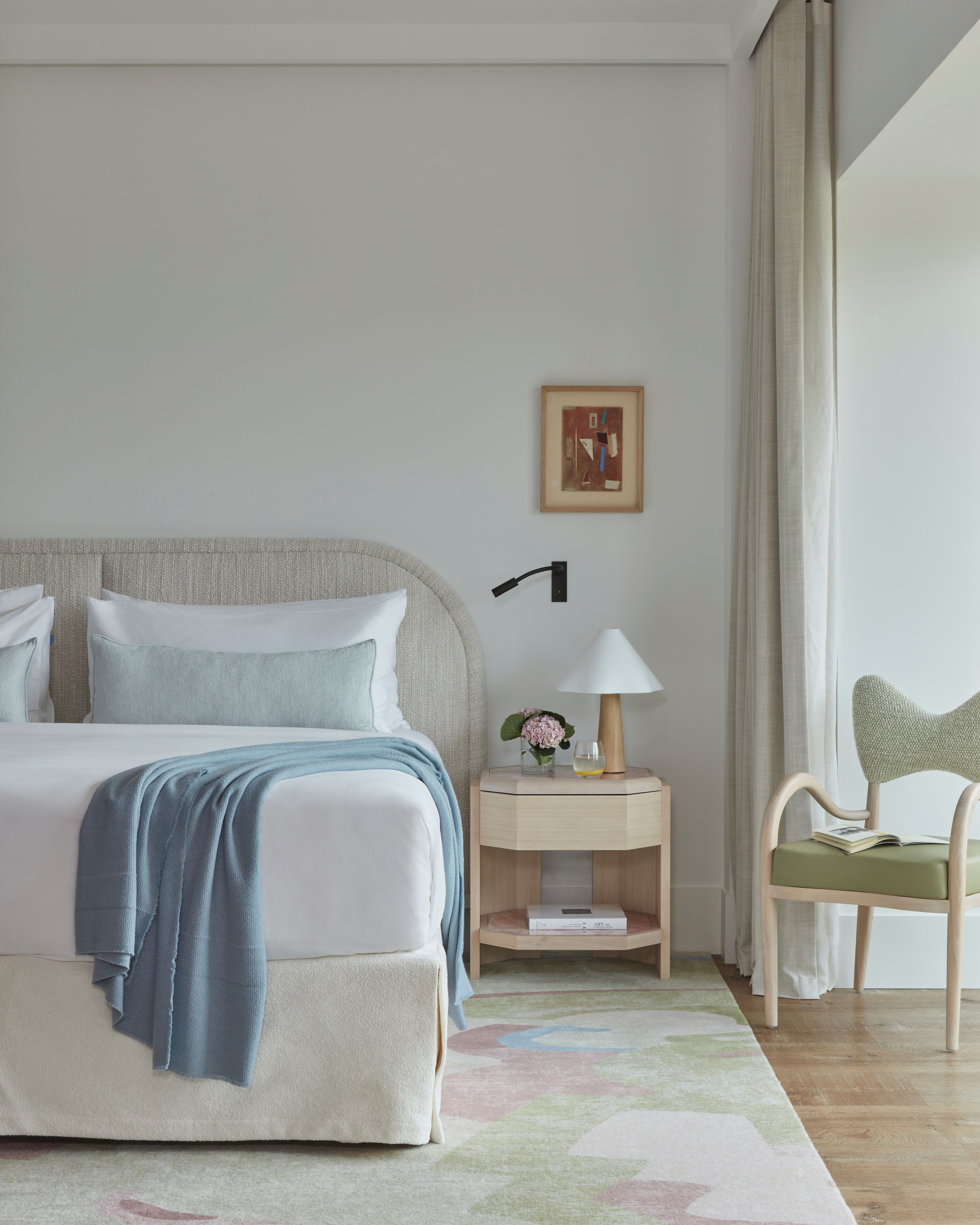 Un dormitorio ordenado con cama, mesita de noche, lámpara, silla y un cuadro en la pared.