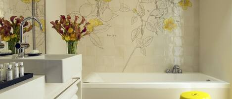 A modern bathroom with a bathtub, a vanity with a mirror, and a yellow stool.