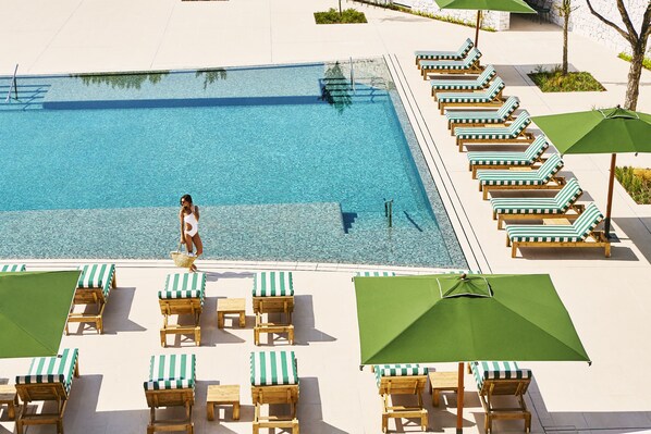 Ein Swimmingpool mit Liegestühlen und Sonnenschirmen, eine Frau in Badebekleidung und ein klarer, blauer Himmel.