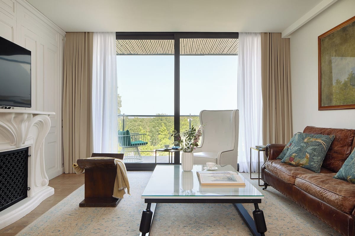 Un salon avec une cheminée, un canapé, une table basse et une grande fenêtre avec des rideaux.